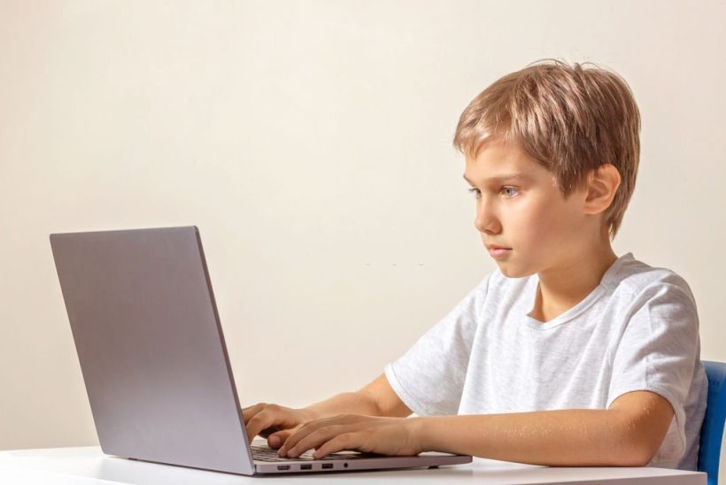 Kid sitting at the table and using laptop computer